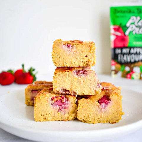 Botanika Blends Plant Protein Oh My Apple Pie lifestyle shot of baked fruit squares topped with strawberries on a plate, with the pouch behind