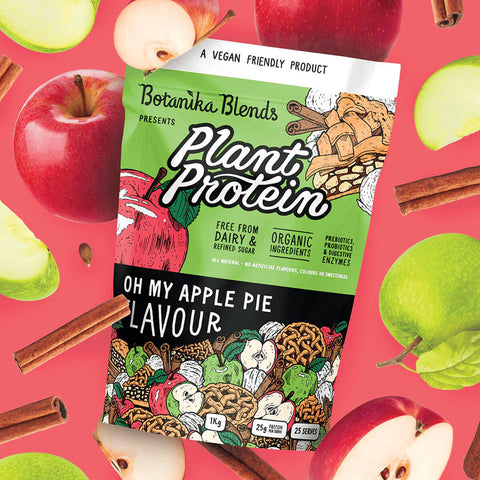 Botanika Blends Plant Protein Oh My Apple Pie lifestyle shot of the pouch among red and green apples and cinnamon sticks on a pink backdrop