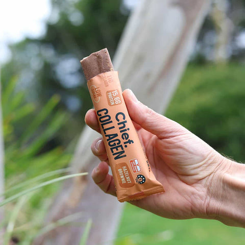 Hand holding a Chief Collagen snack bar with a blurred natural background