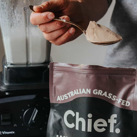 Person holding a spoonful of chocolate whey protein powder to blend into smoothie.