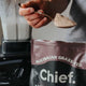 Person holding a spoonful of chocolate whey protein powder to blend into smoothie.
