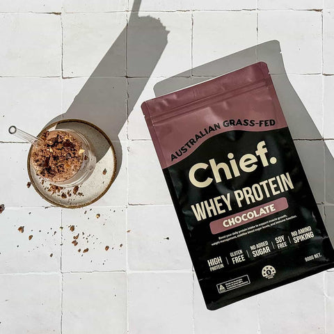 Chief Whey Protein package on a white tiled surface with a glass of chocolate smoothie.