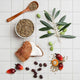 Assorted seeds, nuts, & a coconut on a white grid background.
