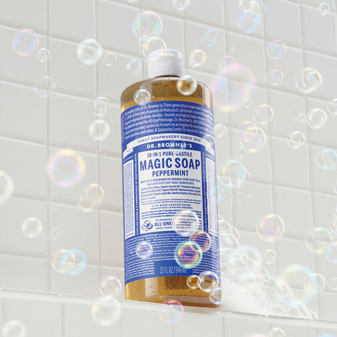 Bottle of Dr. Bronner's 18-in-1 Pure-Castile Magic Soap - Peppermint on a tiled bathroom wall with bubbles.