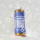 Bottle of Dr. Bronner's 18-in-1 Pure-Castile Magic Soap - Peppermint on a tiled bathroom wall with bubbles.