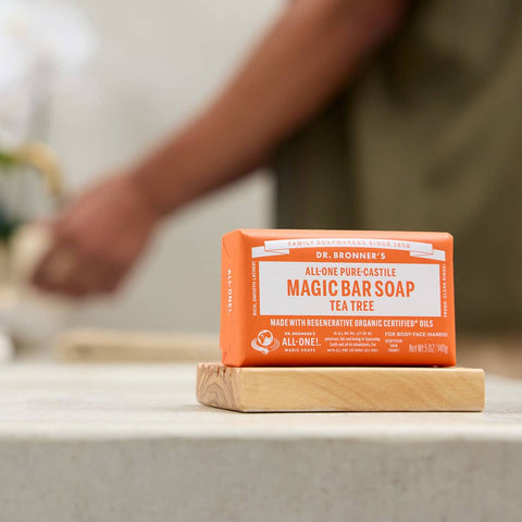 Dr. Bronner's Pure-Castille Magic Soap Bar - Tea Tree 140g on a wooden stand with a blurred background.