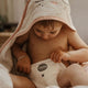 Baby wrapped in a towel, wearing a pull-up with a brand label, sitting on a soft surface.
