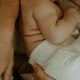 Close-up of a baby in a pull-up nappy being held by a parent.