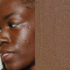 Model next to swatch of Elate Beauty Creme Concealer in the shade 'CN7', for deep neutral skin tones. A two-in-one concealer and illuminator formulated with evening primrose oil, designed to heal and conceal blemishes.
