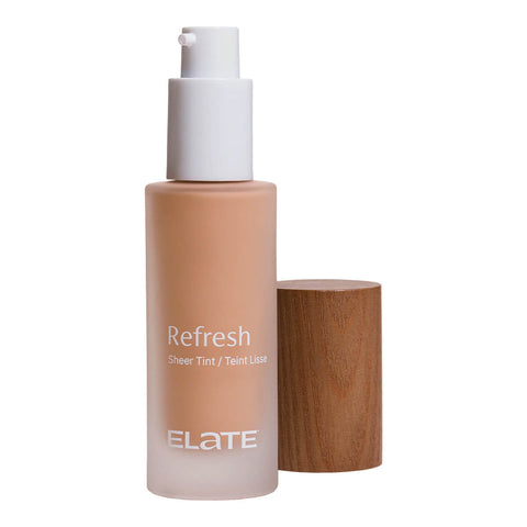 Elate Beauty Refresh Foundation 30ml RN5 in a frosted glass bottle with a white pump and a wooden cap beside it, showing a warm beige tint on white
