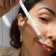 Ere Perez Almond Brow Pencil Perfect 1.1g lifestyle close up of a woman with a gold earring using the pencil and spoolie on her brow