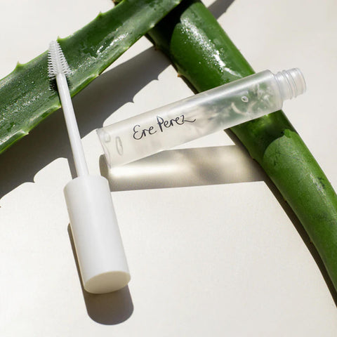Ere Perez Aloe Gel Lash & Brow Mascara Clear 10ml lifestyle shot of the tube and wand lying on green aloe leaves, styled lifestyle photo