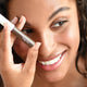 Ere Perez Argan Brow Hero Perfect 3.5ml lifestyle shot of a smiling woman applying the brow gel with the wand, styled lifestyle photo