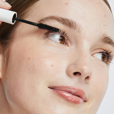 Ere Perez Avocado Waterproof Mascara Black lifestyle close up of a woman's face as the mascara wand brushes her upper lashes, soft light