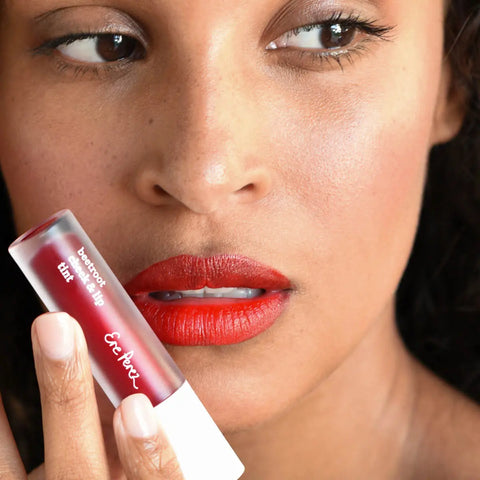 Close-up of a woman's face with red lipstick and tint with lip gloss tube held in front.