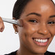Woman applying Ere Perez Cacao Bronzing Pot - Costa 7.5g makeup product with a brush.