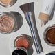 Ere Perez Eco Vegan Brush Multipurpose lifestyle flat lay of the brush beside open pots and a tube of makeup on a pale surface
