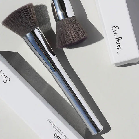 Ere Perez Eco Vegan Brush Multipurpose lifestyle shot of two brushes and a white Ere Perez box lying on a grey surface, styled lifestyle photo