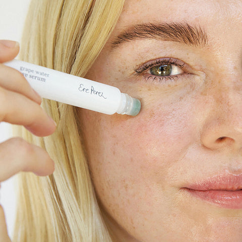 Woman using Ere Perez Grape Water Eye Serum with a jade roller applicator.