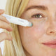 Woman using Ere Perez Grape Water Eye Serum with a jade roller applicator.
