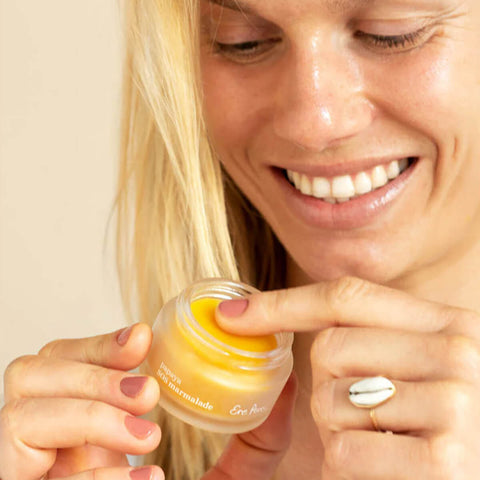 Ere Perez Papaya SOS Marmalade 30g lifestyle shot of a smiling woman with blonde hair holding the open jar of balm, close up shot