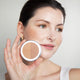 Ere Perez Rice Powder Blush & Bronzer Roma lifestyle close up of a woman with her hair pulled back holding the open compact beside her face