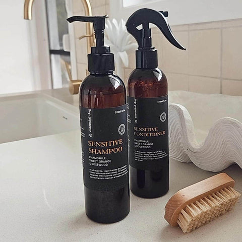 Two bottles of sensitive shampoo and conditioner on a bathroom counter with a brush.