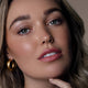 Model wearing brown Eye of Horus Goddess Mascara, a gentle, long-wear, and water-resistant formula that coats lashes without clumping. Infused with moringa oil to promote lash health, and enriched with carnauba, candelilla, rice bran wax, and cera alba to nourish and set the formula for a long-wear, smudge-proof finish. Packaged responsibly in post-consumer resin.
