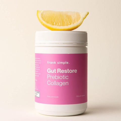 Pink supplement container labeled 'Gut Restore Prebiotic Collagen' 260g from Frank Simple with a lemon wedge on a beige background.
