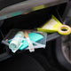 A clear zippered pouch containing a rolled towel, a toothbrush, and a turquoise sponge, resting in a car glove box next to a lime green hand mirror.