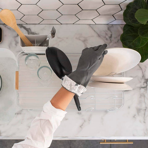 Person wearing black gloves washing dishes in a kitchen with marble countertop and geometric tile backsplash.