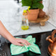Full Circle Renew Essentials Microfibre Cloths 5 pack lifestyle shot of a hand wiping a kitchen bench with a green cloth beside a plant