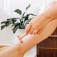 Person using a rose gold razor on their arm with a blurred indoor background.