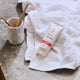 Hair serum tube on a towel with a cup and toothbrushes in the background.