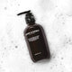 Bottle of gentle gel facial cleanser laying on its side in foamy water.