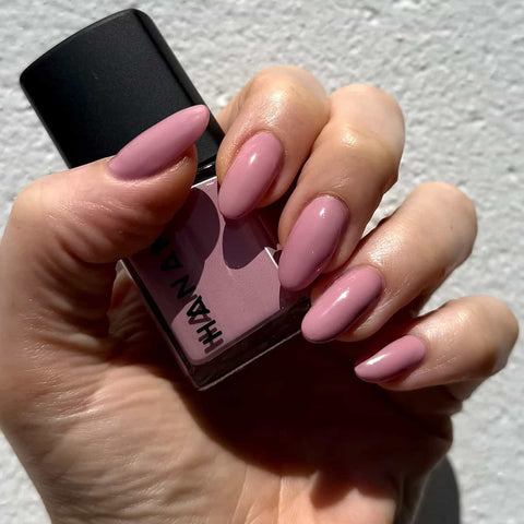 Hand holding a pink nail polish bottle with matching nails against a neutral background