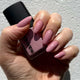 Hand holding a pink nail polish bottle with matching nails against a neutral background