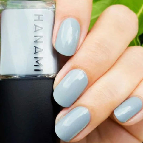 Hand with light blue nails holding a bottle of Hanami nail polish.