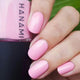Pink nail polish on nails with a bottle of Hanami nail polish in the background.