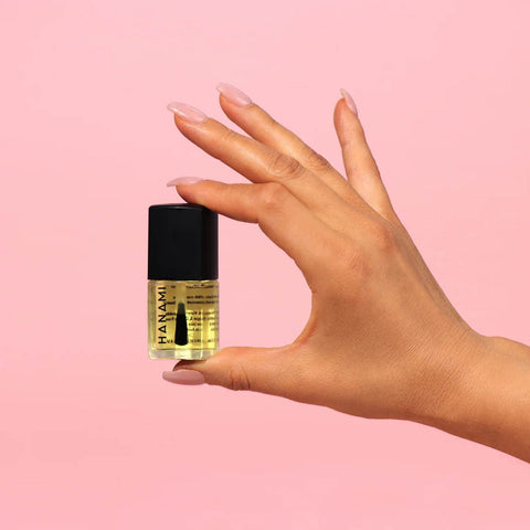 Hand holding a small bottle of Hanami nail polish against a pink background