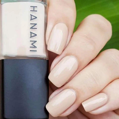 Nail polish bottle with 'HANAMI' branding next to a hand with beige nail polish on a green leaf background