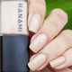Nail polish bottle with 'HANAMI' branding next to a hand with beige nail polish on a green leaf background
