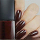 Nail polish bottle with a hand showing dark brown nails