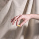 Hand holding a yellow pill against a beige curtain background