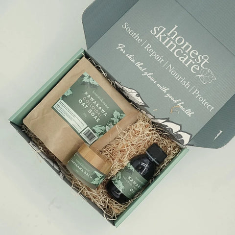 Honest Skincare Kawakawa Balm Healing Gift Set lifestyle shot of an open grey gift box with the balm, oat soak and oil bottle on a bed of straw