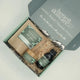 Honest Skincare Kawakawa Balm Healing Gift Set lifestyle shot of an open grey gift box with the balm, oat soak and oil bottle on a bed of straw