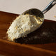 Honest Skincare Kawakawa Balm Healing Gift Set lifestyle shot of a metal scoop of pale oat powder on a dark wooden board, styled lifestyle photo