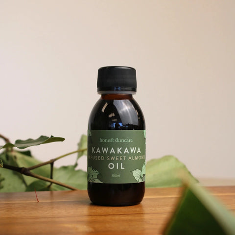 Honest Skincare Kawakawa Balm Healing Gift Set lifestyle shot of the dark oil bottle with a green label among leaves on a wooden table