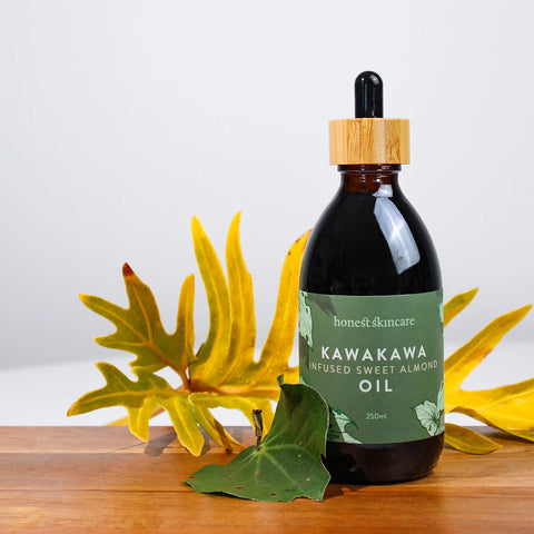 Honest Skincare Kawakawa Infused Sweet Almond Oil 250ml lifestyle shot of the dropper bottle beside yellow flowers and green leaves on wood