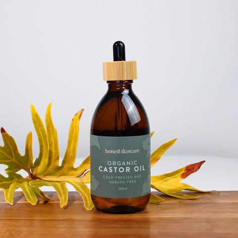 Honest Skincare Organic Castor Oil 250ml lifestyle shot of the dropper bottle on wood beside yellow flowers, styled lifestyle photo